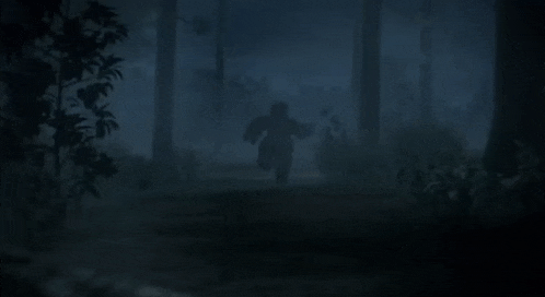 a man in a mask is laying on the ground in a dark forest
