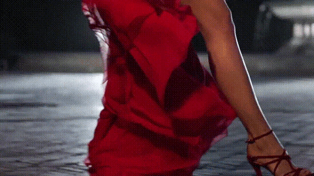 a woman in a red dress and red heels is standing on a sidewalk .