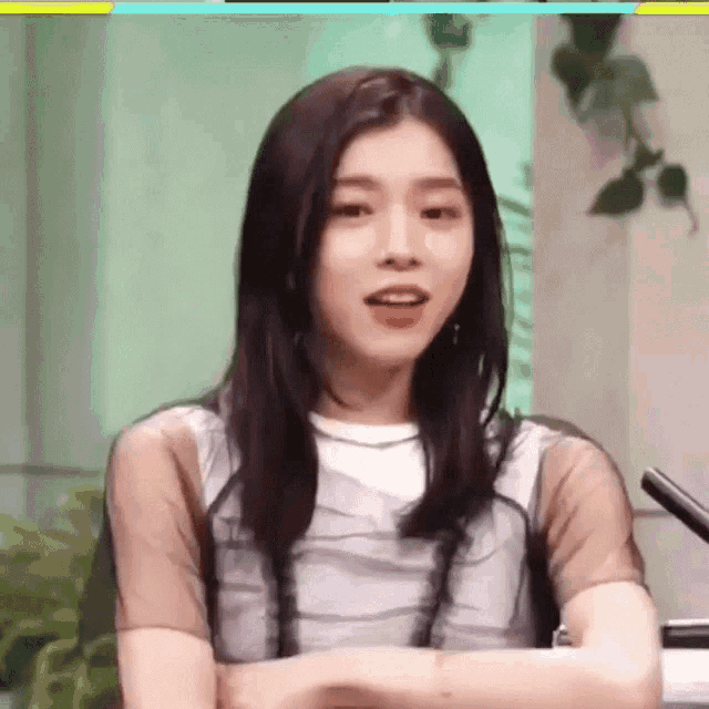 a woman is sitting in front of a microphone with her arms crossed and looking at the camera .