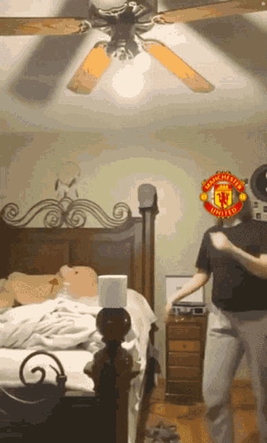 a man dancing in a bedroom with a manchester united logo on his head