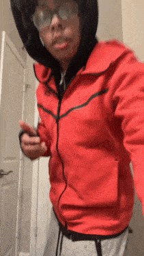 a person wearing a red nike jacket and glasses is standing in front of a door