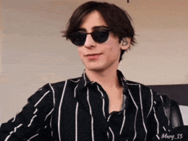 a young man wearing sunglasses and a striped shirt is smiling .
