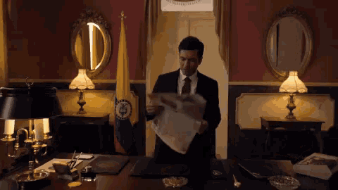 a man in a suit and tie is holding a piece of paper in front of a flag
