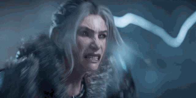 a woman with white hair and a fur coat is screaming with her mouth wide open .