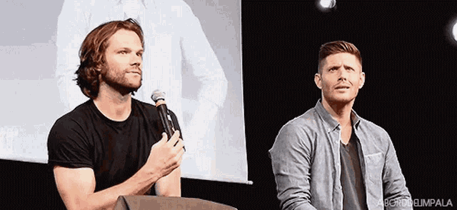 two men are standing next to each other and one is holding a microphone