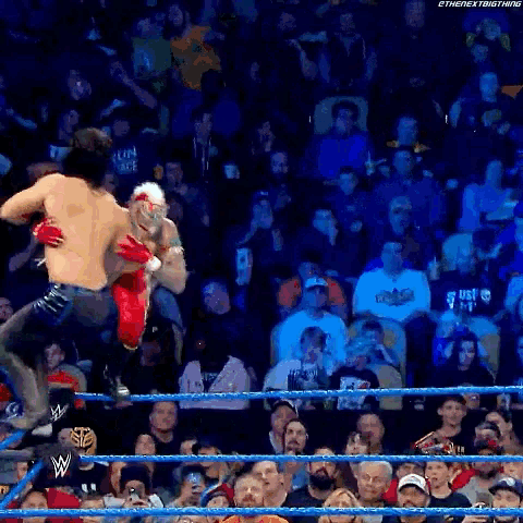 a wrestler is jumping over another wrestler in a crowded stadium