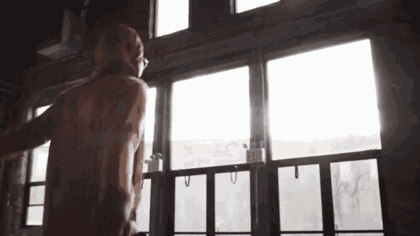 a woman is standing in front of a window with her arms outstretched and the sun is shining through the windows .