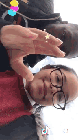 a girl wearing glasses and a red sweater is making a heart with her hands