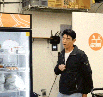 a man in a black jacket is standing in front of a refrigerator with an orange sticker on it