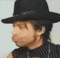 a man wearing a black cowboy hat and a striped shirt is making a funny face .