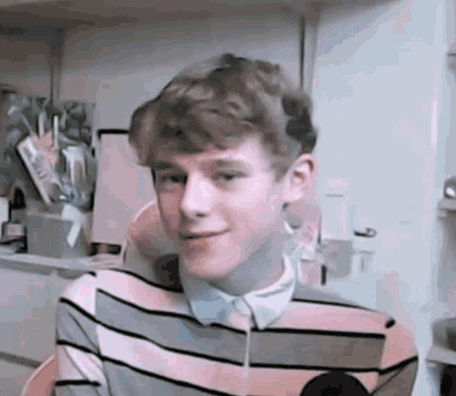 a young man wearing a striped shirt and a white shirt is sitting in a room .