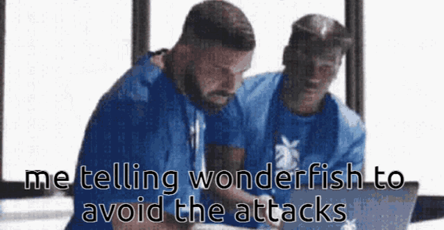two men are sitting in front of a laptop computer . one of the men is telling the other to avoid the attacks .