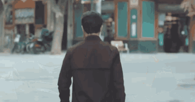 a man in a brown jacket is walking down a street in a city .