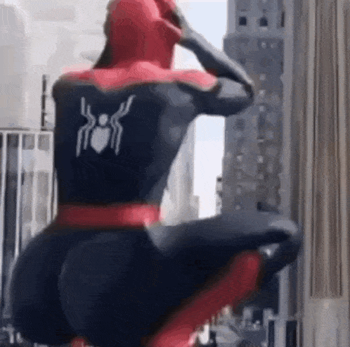 a man in a spiderman costume is squatting down in front of a building .