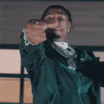 a man wearing a green jacket is pointing at the camera .
