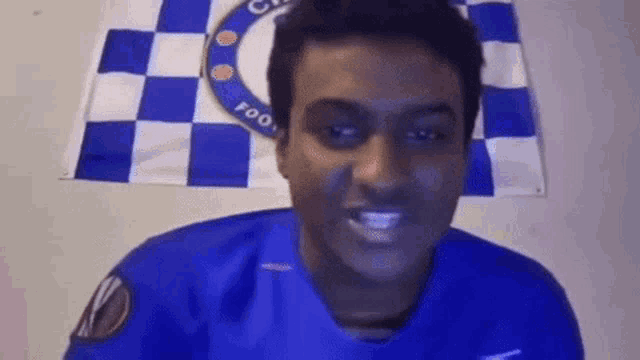 a man wearing a blue shirt is standing in front of a chelsea flag .
