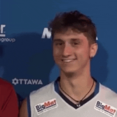 a young man wearing a basketball jersey with a big mat logo on it is smiling .