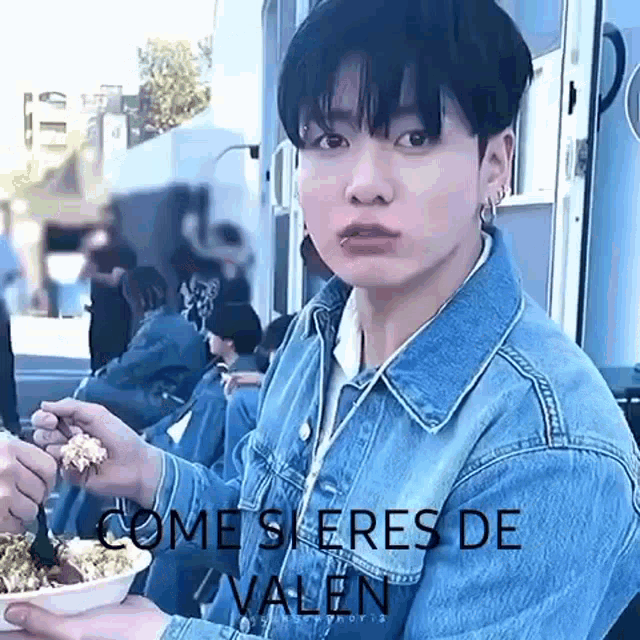 a young man in a denim jacket is holding a bowl of food and making a funny face .