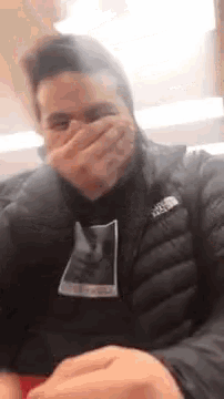 a man wearing a black jacket is covering his mouth with his hand .