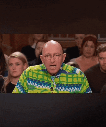 a bald man wearing a colorful shirt and tie stands in front of a crowd of people