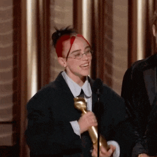 a woman with red hair and glasses is holding a microphone and a trophy .
