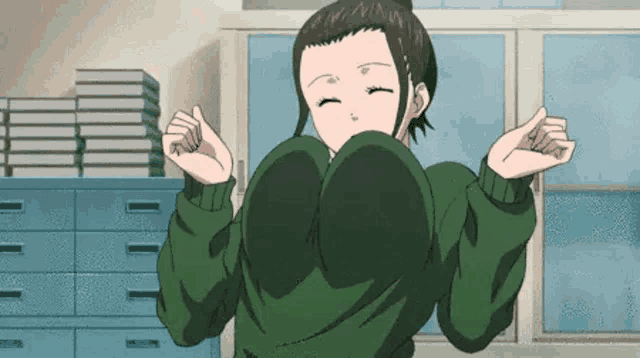 a girl in a green sweater with huge breasts is standing in front of a window .