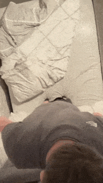 a man in a gray shirt is laying on a bed with a blanket and pillows .
