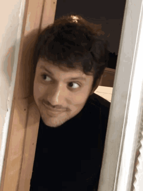 a man in a black turtleneck looks out a doorway