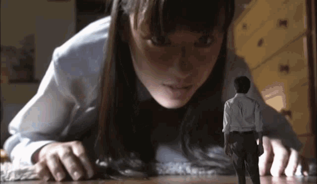 a woman is laying on the floor looking at a small man .