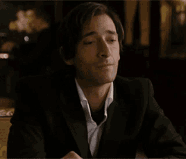 a man in a suit is smiling with his eyes closed in a dark room