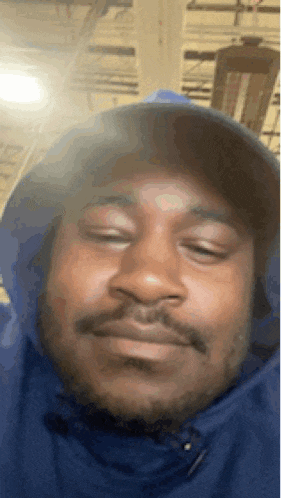 a man wearing a blue hoodie and a hat looks at the camera .