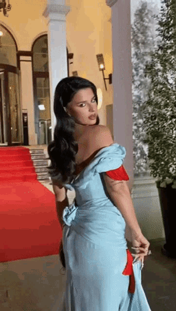 a woman in a blue dress is standing on a red carpet in front of a building