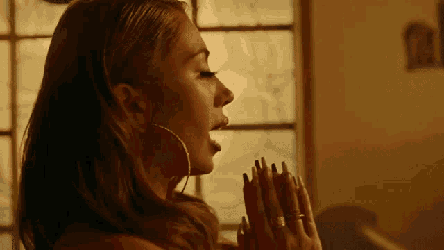 a woman wearing hoop earrings and a ring on her finger is praying