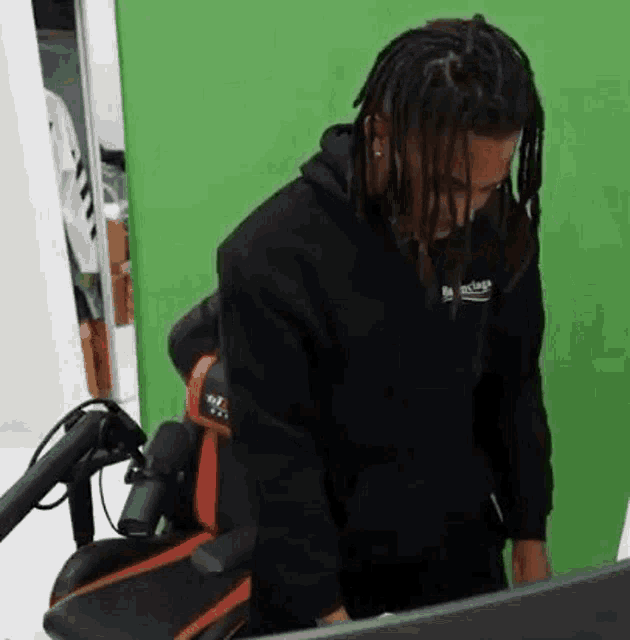 a man with dreadlocks is sitting in a chair in front of a computer monitor .