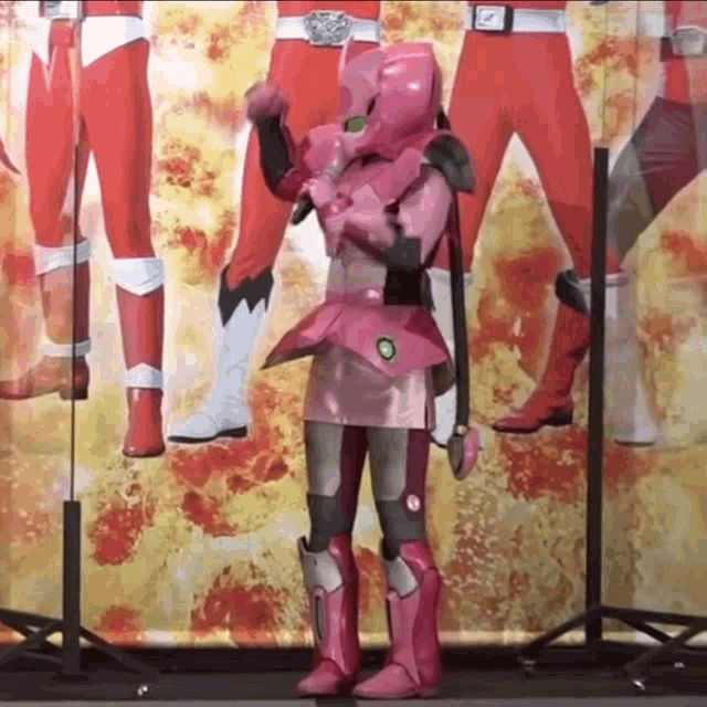 a woman in a pink superhero costume is standing in front of a group of red superhero posters .