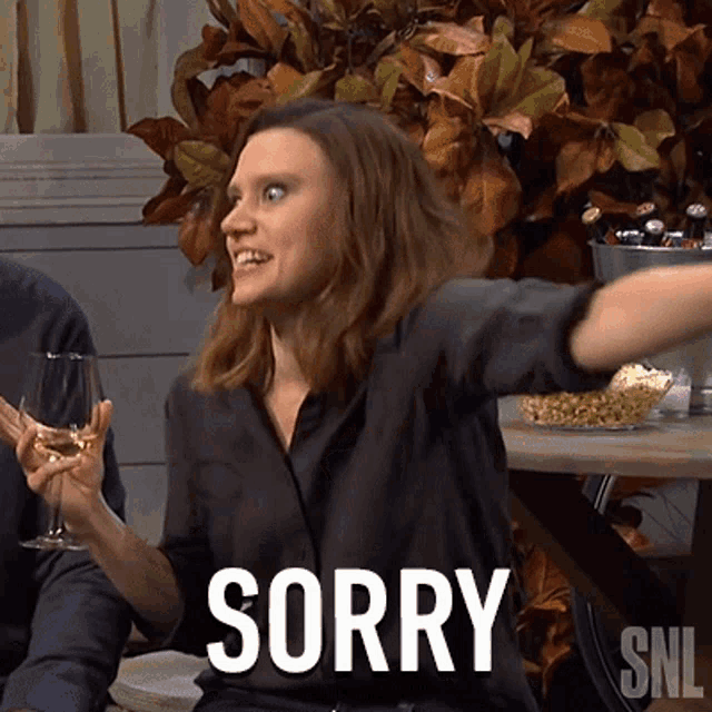 a woman in a black shirt is holding a glass of wine and says sorry snl