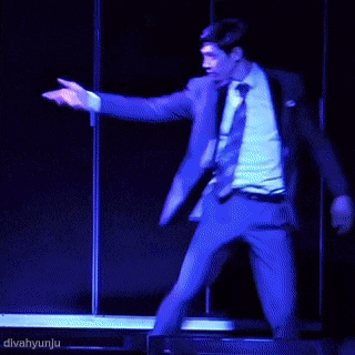 a man in a suit and tie is dancing on a stage with divahyunju in the corner