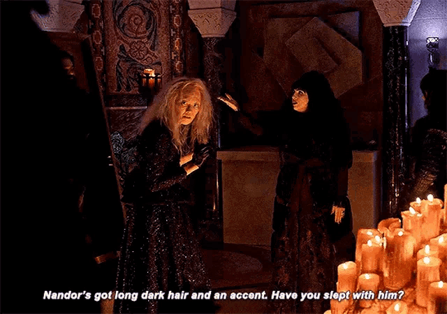 two women are standing in front of a table full of candles and one of them says nandor 's got long dark hair