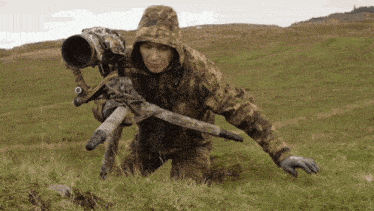 a man in a camo jacket holds a camera on a tripod in a field