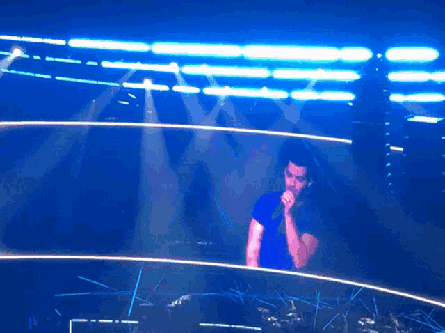 a man singing into a microphone in front of a blue light