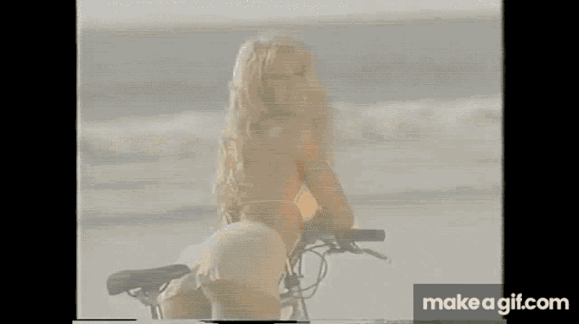 a woman in a pink bikini is riding a bike on the beach
