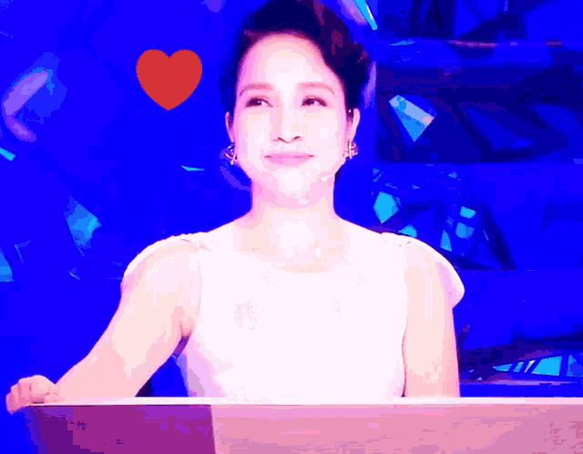 a woman in a white dress stands in front of a blue background with a red heart above her head