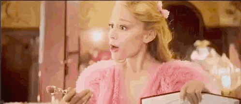 a woman in a pink dress is holding a bottle of perfume in her hand .
