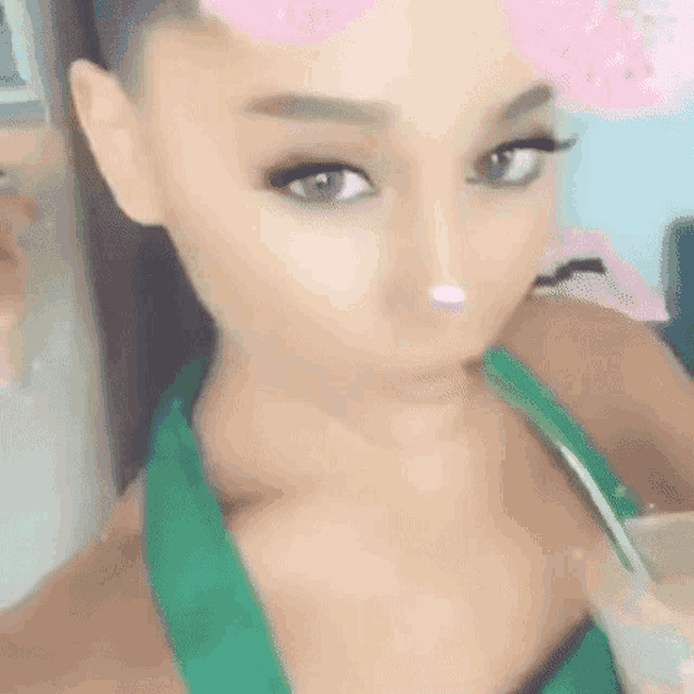 ariana grande is wearing a green top and taking a selfie with a flower on her nose .