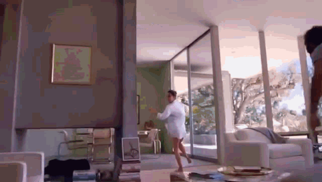 a woman in a white shirt is dancing in a living room with a lot of windows