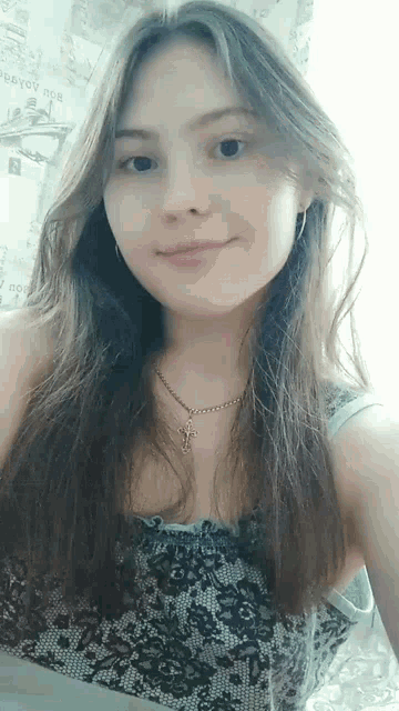 the girl is wearing a necklace with a cross on it and is smiling for the camera .