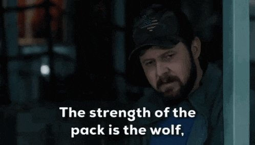 a man with a beard wearing a hat and a blue shirt says the strength of the pack is the wolf