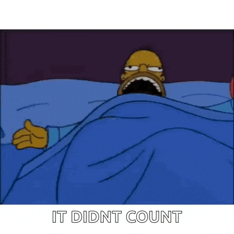 homer simpson is laying in bed under a blue blanket with his mouth wide open .