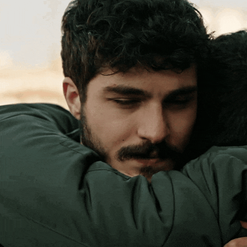 a man with a beard and mustache is hugging another man in a green jacket