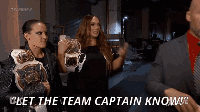 two women holding championship belts are standing next to a man who says " let the team captain know !! "